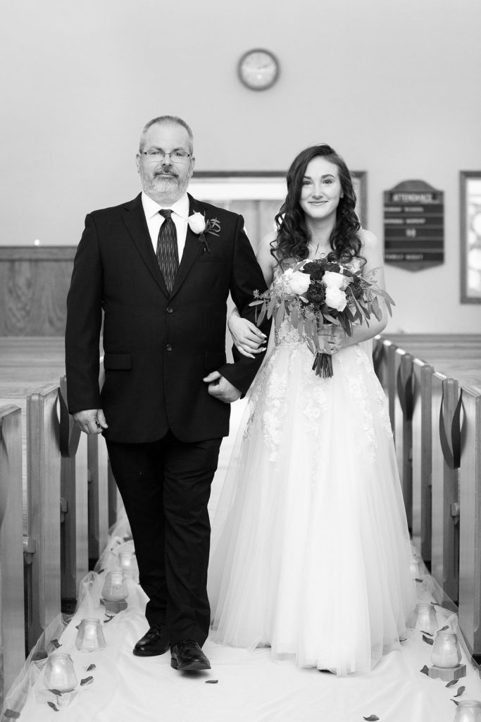 dad walks bride up the aisle during a wedding at Trinity Missionary Church in Yale, Michigan