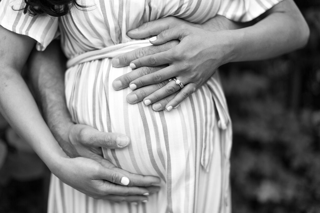 husband and wife's hands holding pregnant belly